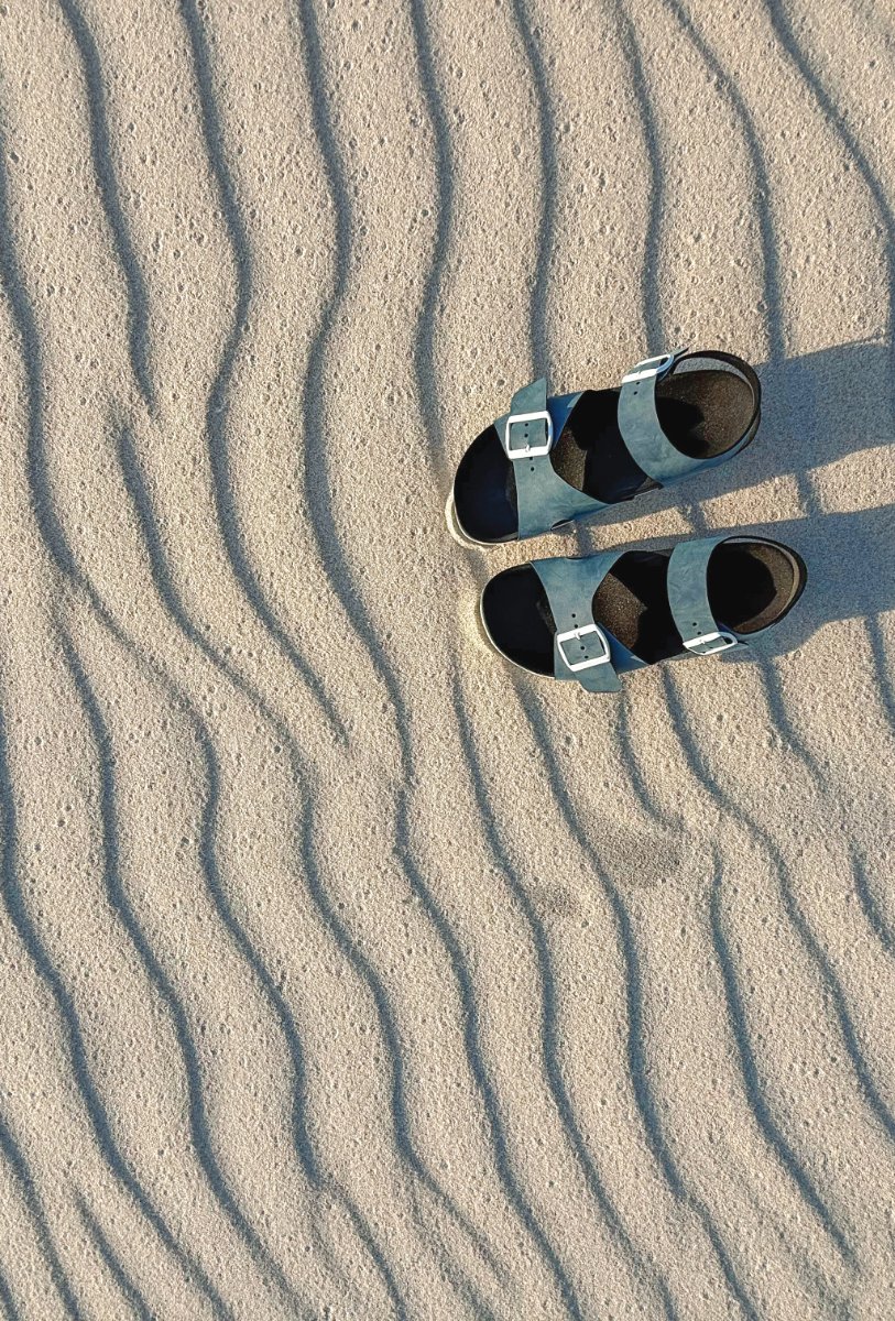 Maatwerksandalen op het zand, van boven gefotografeerd